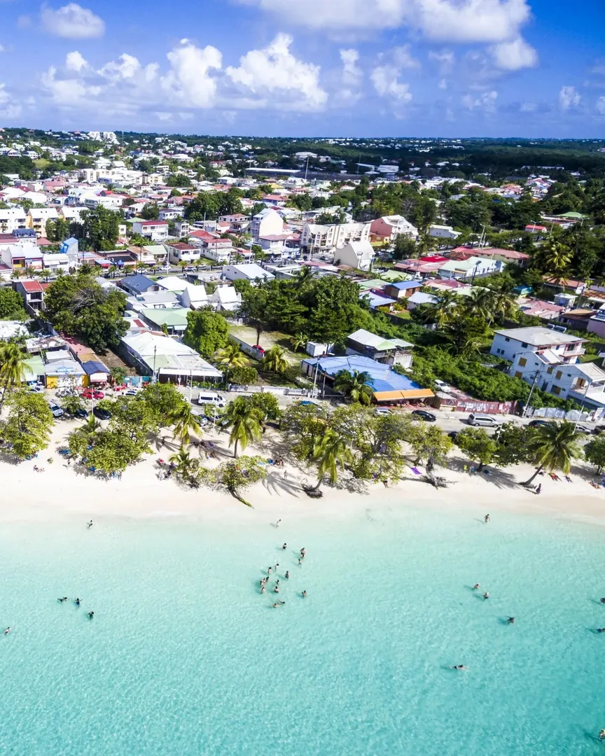 Vue du bourg de Sainte-Anne depuis la plage : la rue commerçante longeant le sable blanc et les terrasses de restaurants.